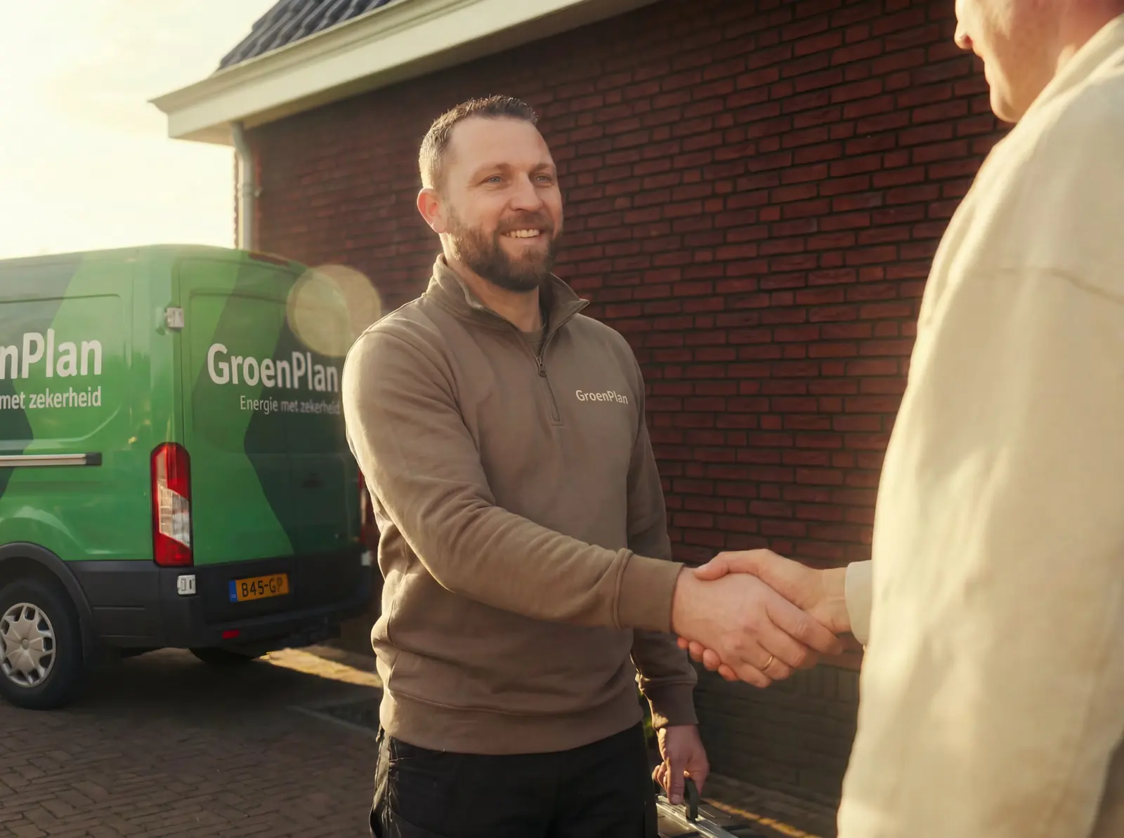 Een monteur van GroenPlan geeft een klant een hand bij de GroenPlan-bus